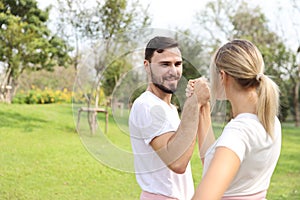 Image of young caucasian couple in white and pink sport dress with smiling and arm wrestling challenge in the park with green tree