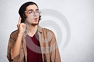 Image of young caucasian hipster man wearing glasses, maroon shirt, jacket and cap, posing isolated over white background,