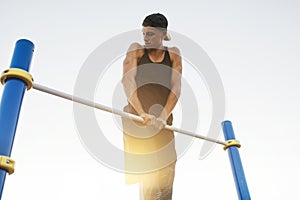 Image of young Caucasian muscular male doing pull ups exercises on horizontal bar outdoors. Athletic runner training hard at sunny