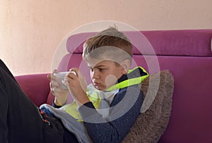 Image of young cute boy playing games on mobile phone lounging on sofa