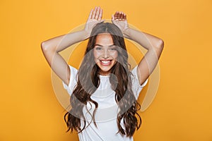 Image of young european woman 20s with long hair smiling and showing rabbit ears at her head, isolated over yellow background