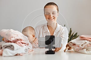 Image of young female blogger broadcasting livestream at home together with her infant daughter, filming content for her blog,