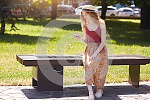 Image of young girl charges mobile phone via USB outdoors, female sitting on bench with solar panel in town park. Public charging