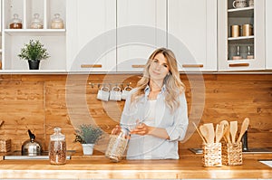 Image of young happy lady standing in kitchen while cooking fish. Looking at camera photo