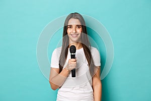 Image of young happy woman in white t-shirt, giving a speech, holding microphone to sing or perform, standing over blue