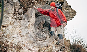 Image of young male hiking in mountains wearing red clothes exploring new place. Traveler man trekking and mountaineering