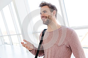 Image of young man smiling while standing over bright window indoors