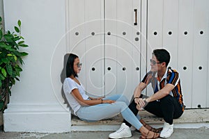 Image of a young man and woman dressed informally talking while sitting outdoors photo