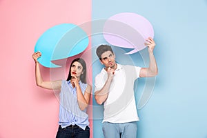 Image of young man and woman holding copyspace bubbles for advertisement, isolated over colorful background
