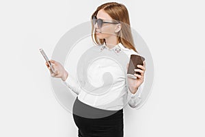 Image of a young pregnant businesswoman wearing glasses, a girl holding a smartphone and drinking coffee in a Cup