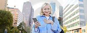 Image of young professional, office manager woman with backpack and smartphone, posing on streets of busy city, holding