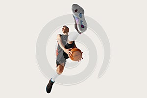 Image of young streetball player wearing sport clothes jumping over with ball over white background