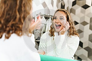 Image of young woman applying moisturizing facial cream in bathroom