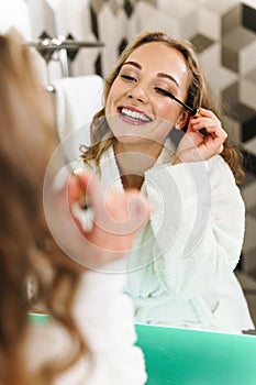 Image of young woman in housecoat applying makeup after shower in bathroom photo