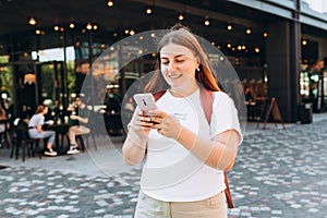 Image of young woman outdoors on the street chatting by mobile phone. Young women with backpack using smartphone at the