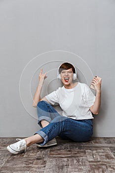 Image of young woman showing horn finger and using cellphone on floor