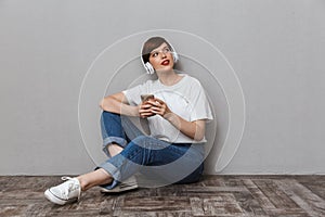 Image of young woman using cellphone and headphones sitting on floor