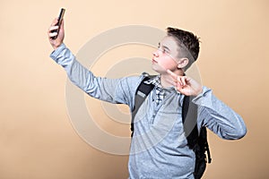 Image of youngster guy wearing casual clothing and backpack holding smartphone and taking selfie isolated over beige background