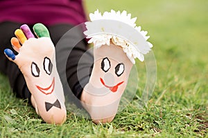 Images of lovely groom and bride just married painted in bright colors on feet of child outdoor at summer.