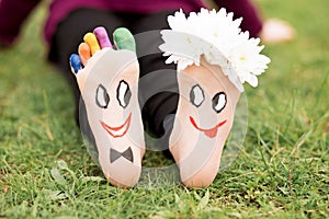 Images of lovely groom and bride just married painted in bright colors on feet of child outdoor at summer.