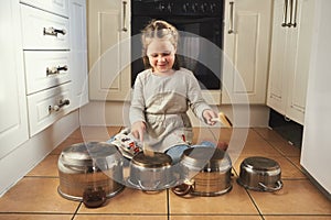 Imagination is her favourite toy. a little girl playing drums on a set of pots in the kitchen.
