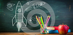 Imaginative education concept with rocket drawing on chalkboard, books and apple