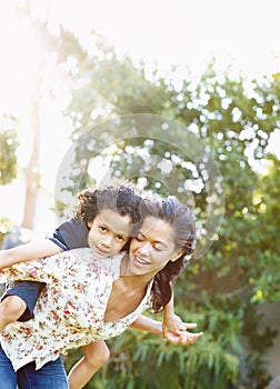 Imagining theyre flying. A young mother piggybacking her son in the park.