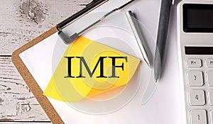 IMF word on yellow sticky with calculator, pen and clipboard