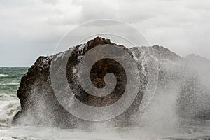 Immense sea rock covered by a large wave. Force of nature