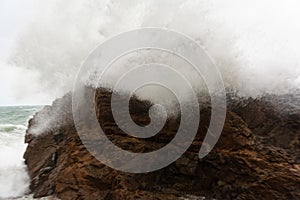 Immense waves hitting a large rock at the edge of the beach. Force of nature