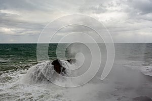 Immense waves hitting a large rock at the edge of the beach. Force of nature