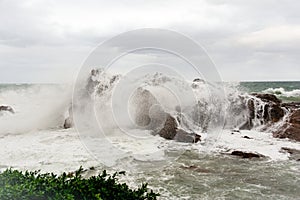 Immense waves hitting a large rock at the edge of the beach. Force of nature