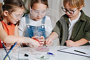 Immersed little kids doing home science project, filling glass dish