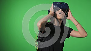 Immersion in virtual reality. Portrait of a young girl on a green background wearing virtual reality glasses looking at