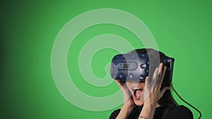 Immersion in virtual reality. Portrait of a young girl on a green background wearing virtual reality glasses, who is