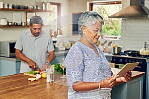 Immortalizing her secret recipes with smart technology. a mature woman using a digital tablet while preparing a meal at