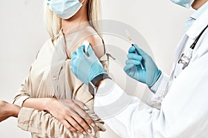 Immunisation. Cropped close up shot of male doctor in blue sterile gloves injecting vaccine to a young woman wearing