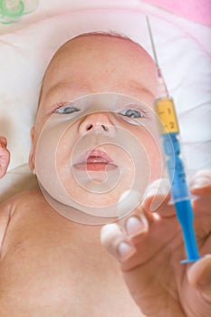 Immunization concept - baby starring on syringe with vaccine for