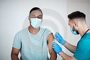 Immunization and health care system. Black male patient visiting doctor, receiving covid-19 vaccine injection at clinic