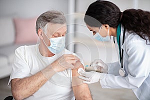 Immunizing homebound patients with covid-19 vaccine. Young doctor giving injection against covoravirus to elderly man photo