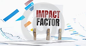 impact factor text on paper sheet with chart, dice, spectacles, pen, laptop and blue and yellow push pin on wooden table -