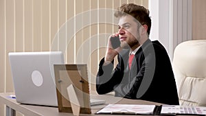 Impatient businessman in black suit and red tie talks on the phone