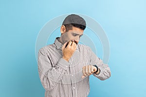 Impatient businessman pointing finger on his wrist watch with nervous face, time is out, deadline.