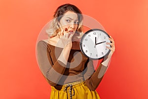 Impatient nervous woman holding big wallclock and biting her nails, need more time for work, deadline photo