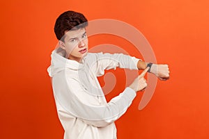 Impatient young man in stylish white sweatshirt with serious face pointing his finger on handwatch, time to act, deadline