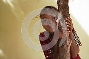 Impishly Smiling Little African Girl Hugging a Tree Trunk