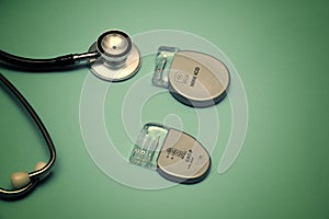 Implantable pacemaker devices such as ICD and CRT devices placed along with a stethoscope on a gradient green background
