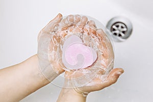 Importance of personal hygiene care. Flat lay view of child washing dirty hands with pink heart shape soap bar, lot of foam. Copy