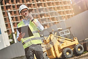 Important call. Young civil engineer or construction supervisor wearing helmet talking by phone while inspecting