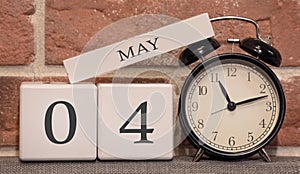 Important date, May 4, spring season. Calendar made of wood on a background of a brick wall. Retro alarm clock as a time